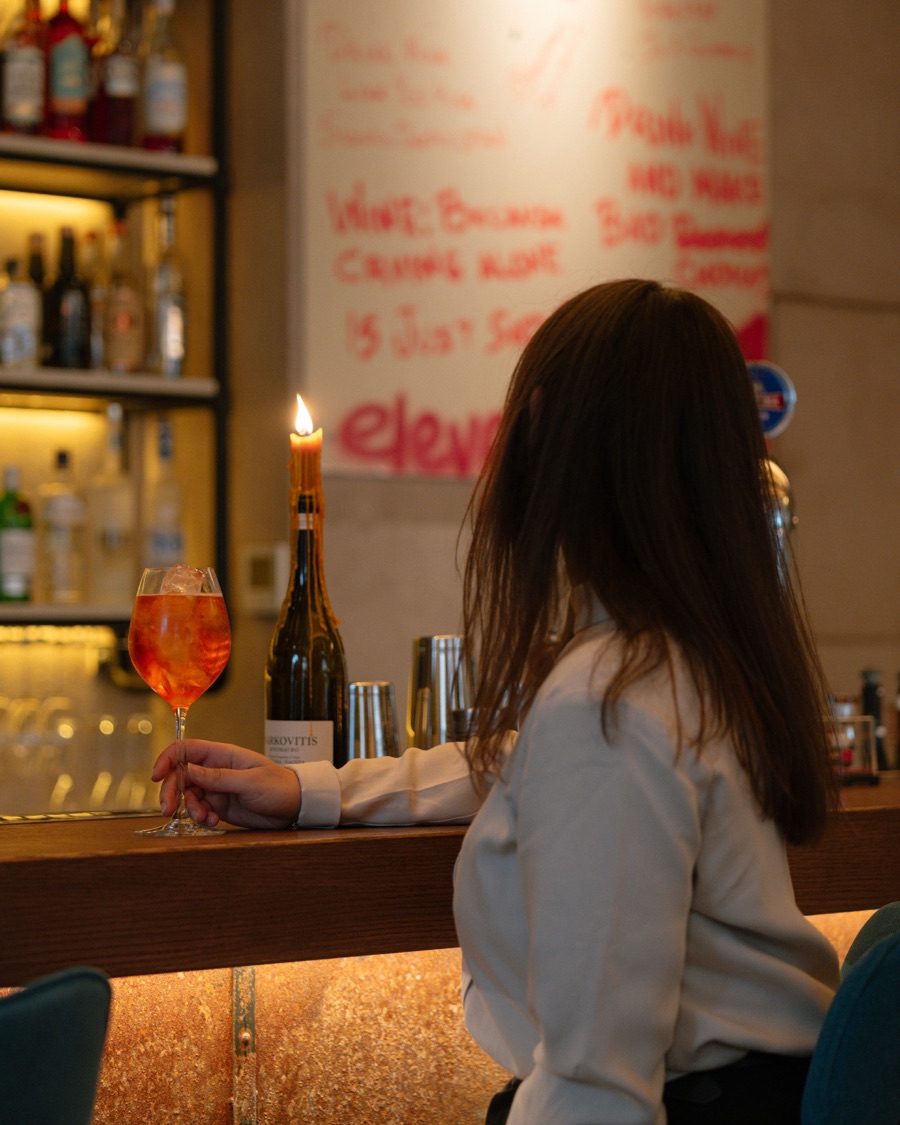 A guest at the Eleve bar with an orange spritz, a candle in a wine bottle beside her