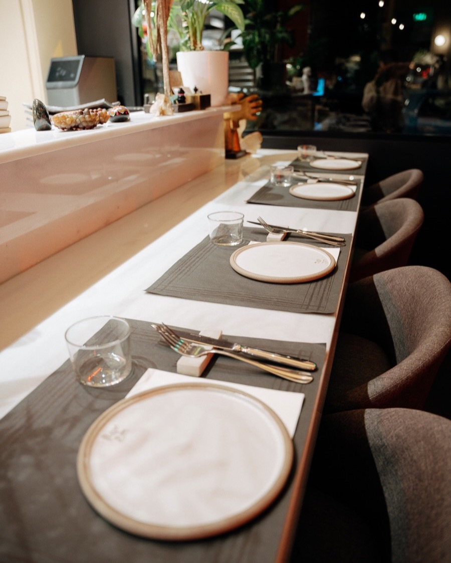 The chef's table at Raw Bata set for service: plates, glasses and chairs along a marble counter